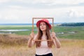 Girl in pink straw hat holds empty wooden picture frame in hands on nature landscape background portrait. Creative idea Royalty Free Stock Photo