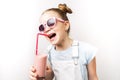 A girl in pink sunglasses drinks a cocktail through a pink straw and laughs merrily.