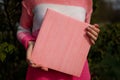 Girl in pink sweater holding photobook or photoalbum with leather pink cover and wooden texture.