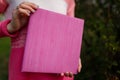 Girl in pink sweater holding photobook or photoalbum with leather purple cover and wooden texture.