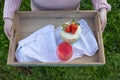 Girl with a pink sweater holding a wooden tray with strawberry sponge cake and red drink on it