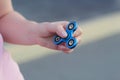 Girl in pink t-shirt is playing blue metal spinner in hands on the street, woman playing with a popular fidget spinner toy, anxiet