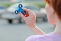 Girl in pink t-shirt is playing blue metal spinner in hands on the street, woman playing with a popular fidget spinner toy, anxiet
