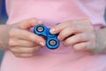 Girl in pink t-shirt is playing blue metal spinner in hands on the street, woman playing with a popular fidget spinner toy