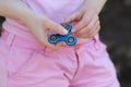 Girl in pink t-shirt is playing blue metal spinner in hands on the street, woman playing with a popular fidget spinner toy