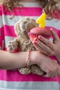 A girl in a pink and white shirt holding a small teddy bear and a pink cupcake with a candle with the number four, close-up