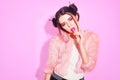 Girl in pink with win buns eats Chupa Chups. Portrait of a pretty young girl eating lollipop over pink background. Lovely smiling Royalty Free Stock Photo