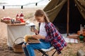 A girl in a plaid shirt reads a book against the background of a tent