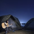 Girl playing guitar at tent glows under a night sky Royalty Free Stock Photo