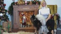 Girl playing with husky sitting on the armchair near the fireplace and Christmas tree. Playful dogs and their owner.