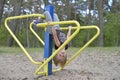 A girl is playing on the playground on the yellow metal attraction. It's windy.