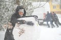 a girl is playing with snow on the street, making a snowman, on background a car is stuck in snow and men are pushing, it is Royalty Free Stock Photo