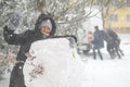 a girl is playing with snow on the street, making a snowman, on background a car is stuck in snow and men are pushing, it is Royalty Free Stock Photo