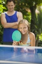 Girl (7-9) playing table tennis with father in background. Royalty Free Stock Photo