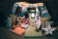 Girl playing with teddies in a tent made of bed sheets and chairs