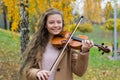 Girl playing the violin in the autumn park at a yellow foliage background Royalty Free Stock Photo