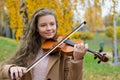 Girl playing the violin in the autumn park at a yellow foliage background Royalty Free Stock Photo