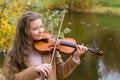 Girl playing the violin and smiling in the autumn park at a lake background Royalty Free Stock Photo