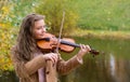 Girl playing the violin and smiling in the autumn park at a lake background Royalty Free Stock Photo