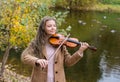 Girl playing the violin and smiling in the autumn park at a lake Royalty Free Stock Photo