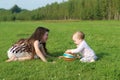 Girl plays with baby and ball on green field at summer