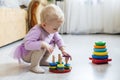 girl plays logical pyramid on floor in living room on sunny day. Montessori wooden toy folded pyramid. Circle, quadra, triangle,