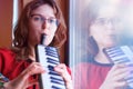 The girl plays melodica. In the hands of a woman musical instrument harmonica. The musician stands at the window. Harmonica with Royalty Free Stock Photo