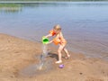 A girl plays on a sandy beach on the shore of a lake in the summer heat. Royalty Free Stock Photo