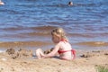 A girl plays on a sandy beach on the shore of a lake in the summer heat. Royalty Free Stock Photo