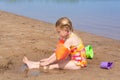 A girl plays on a sandy beach on the shore of a lake in the summer heat. Royalty Free Stock Photo