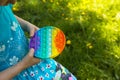 Girl plays with touch anti-stress silicone pop it toy outdoor in the garden. Fingers press on rainbow soft bubbles and buttons.