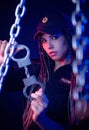 A girl in a police uniform with dreadlocks in neon light with chains and handcuffs English translation the police