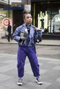 Girl with a ponytail in a blue silk shiny jacket and trousers with pockets, jewelry with a succulent in a pot posing