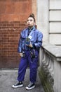 Girl with a ponytail in a blue silk shiny jacket and trousers with pockets, jewelry with a succulent in a pot posing