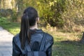 Girl with ponytail is walking in the park. Young girl student stands in the park. Back view