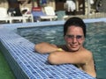 Girl in the pool outdoors. Leaned on board the pool. Smiling, sunglasses on his head