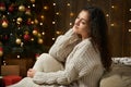 Girl portrait in christmas lights and decoration, dressed in white sweater and stockings, fir tree on dark wooden background, wint Royalty Free Stock Photo