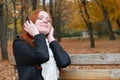 Girl portrait, listen music on audio player with headphones, sit on bench in city park, autumn season, yellow trees and fallen lea Royalty Free Stock Photo