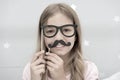 Girl pose with photo booth props glasses and mustache in bedroom. Child girl with party glasses. Child imitate