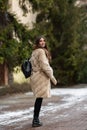 Girl posing on road on winter background. Glamorous funny young woman with smile wearing stylish creamy long fur coat