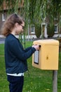 Girl posting a letter into a yellow postbox Royalty Free Stock Photo