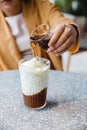 A girl is pouring a shot of espresso in frozen milk mixed with coffee jelly on granite top table. Coffee aroma.