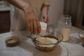 The girl pours the flour into the dough from the glass. The girl prepares the dough for the cake