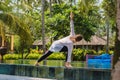 Girl is practicing yoga on the edge of swimming pool with green plants and palm trees around, stretching legs Royalty Free Stock Photo