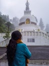 Girl praying at buddhist shanti stupa covered with misty fog at morning from different angle