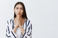 Girl praying god, asking for mercy and luck. Portrait of focused good-looking young woman in striped blouse, holding Royalty Free Stock Photo