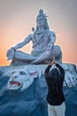 Girl praying at hindu god lord shiva statue in meditation posture with dramatic sky at evening Royalty Free Stock Photo