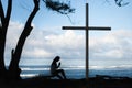 Girl praying to God in front of a cross with a beautiful blue ocean background. Royalty Free Stock Photo