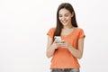 Girl prefers to talk via messages. Studio shot of satisfied carefree beautiful woman in orange t-shirt, holding Royalty Free Stock Photo