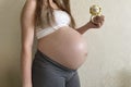 A girl pregnant at the ninth month holds a knitted rattle in the form of a lion in her hands on a monochrome light background. An
